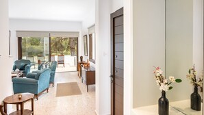 A spacious living area with a sofa, chairs, and a coffee table. There is a door leading to a bathroom with a mirror and two vases.