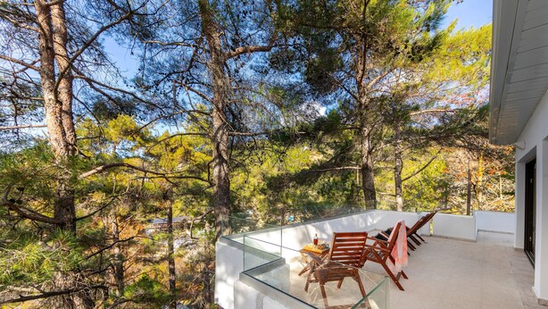 A glass-enclosed balcony with outdoor furniture, surrounded by trees.