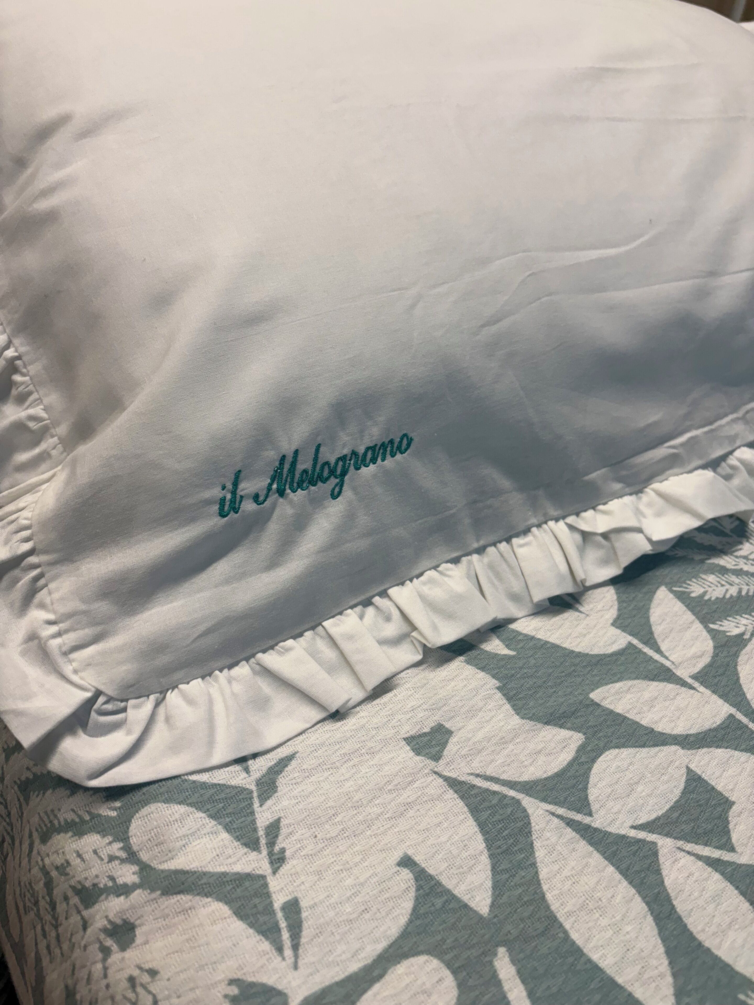 A pillow with a ruffled edge and the text 'il Melograno' embroidered on it.