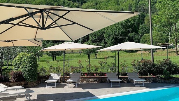 A swimming pool with lounge chairs and umbrellas, surrounded by a landscaped garden and a hilly backdrop.