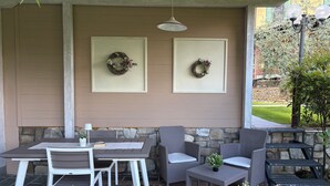 An outdoor patio with a table and chairs, stone walls, and two framed wreaths on the wall.