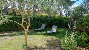 A garden with two metal chairs, a tree, and a hedge. - Gîte LES OLIVIERS located in a quiet area among the pines, close to the beaches (Béziers)