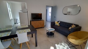 A modern living room with a dining table, sofa, and a TV. - Gîte LES OLIVIERS located in a quiet area among the pines, close to the beaches (Béziers)