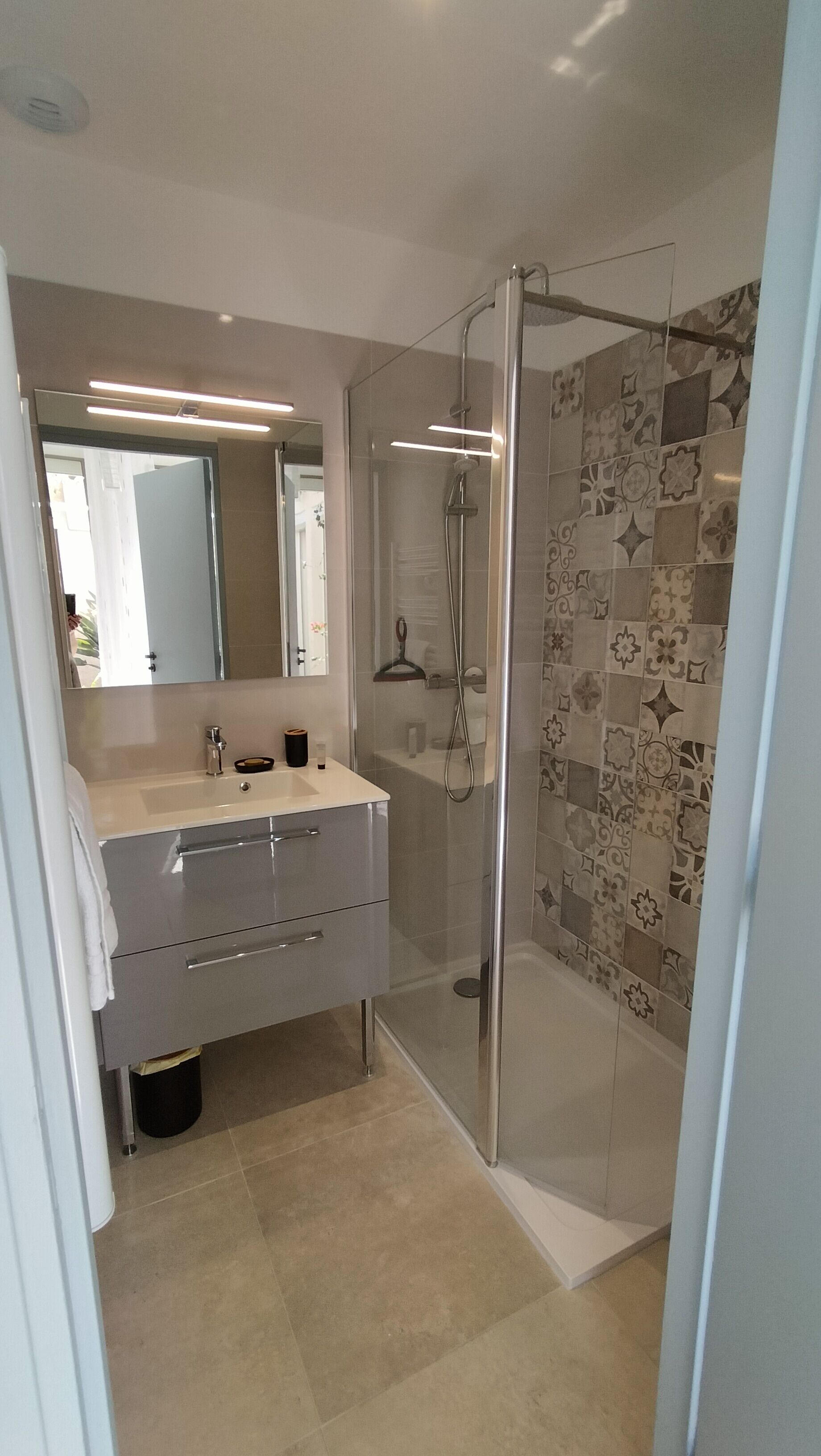 Een moderne badkamer met een glazen douchecabine, een wastafel met spiegel en decoratieve tegels op de wanden.