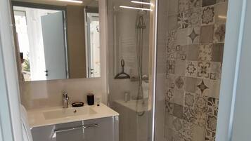 Een moderne badkamer met een glazen douchecabine, een wastafel met spiegel en decoratieve tegels op de wanden.