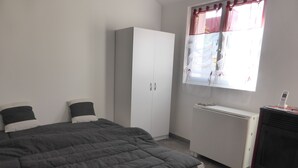 Un dormitorio con cama, armario, radiador y ventana con cortinas.