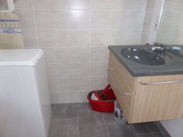 A bathroom with a white toilet, a sink with a wooden cabinet, and a red cleaning bucket.