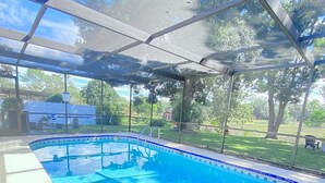 A covered swimming pool with clear blue water, surrounded by a metal frame and glass panels. - Cheerful 1 bedroom guest suite with pool and yard (Spring Hill)