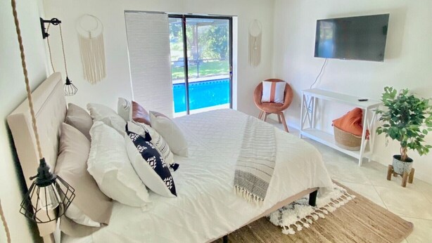 A modern bedroom with a large bed, a TV mounted on the wall, and a view of the outdoors through the sliding doors. - Cheerful 1 bedroom guest suite with pool and yard (Spring Hill)