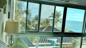 A room with a bed, a lamp, and a view of the ocean through large windows. - Casa Paraiso Caribe - stunning views! (Isla Mujeres)
