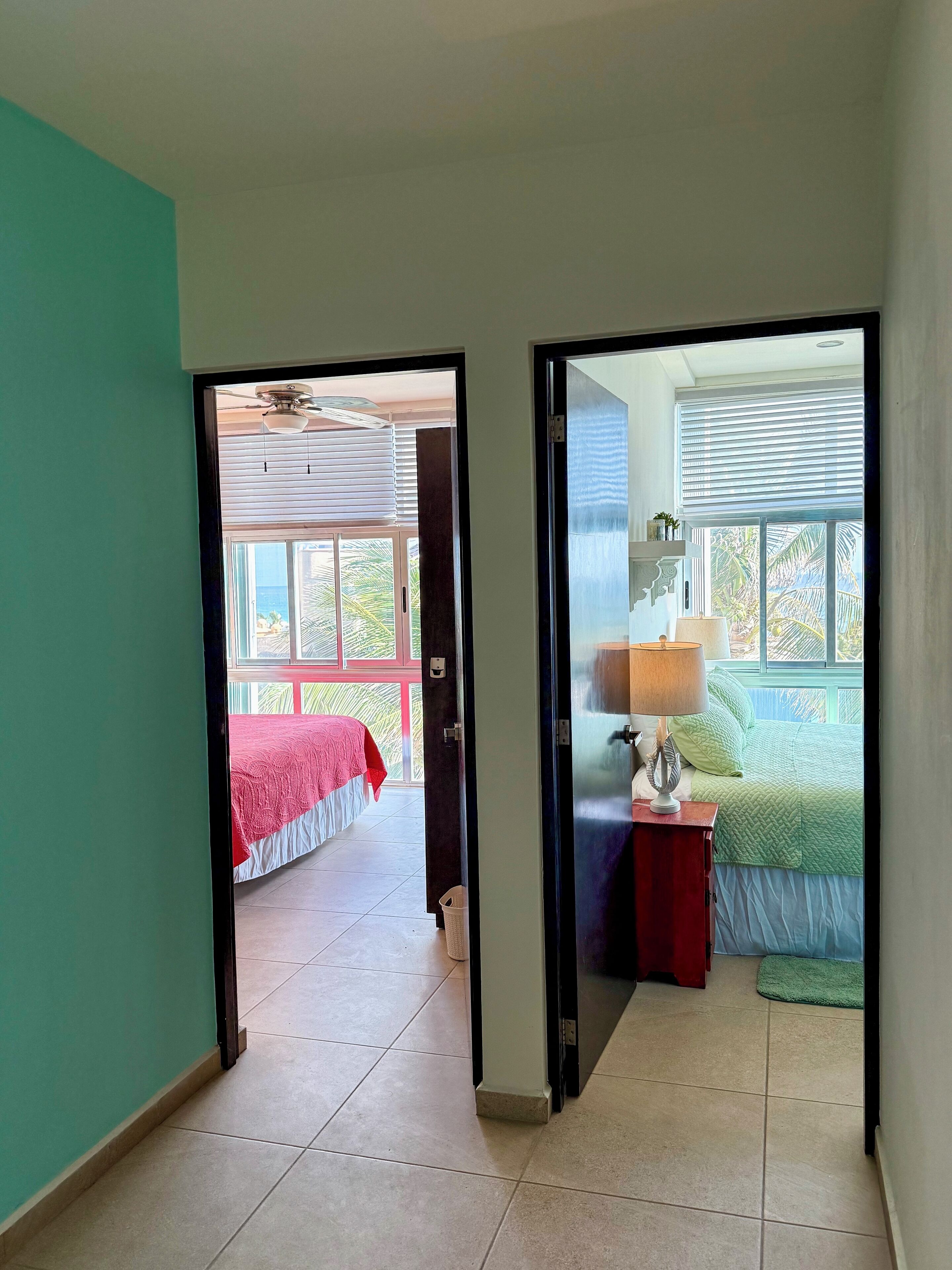 A hallway leading to a bedroom with a bed, a nightstand, and a window with blinds.