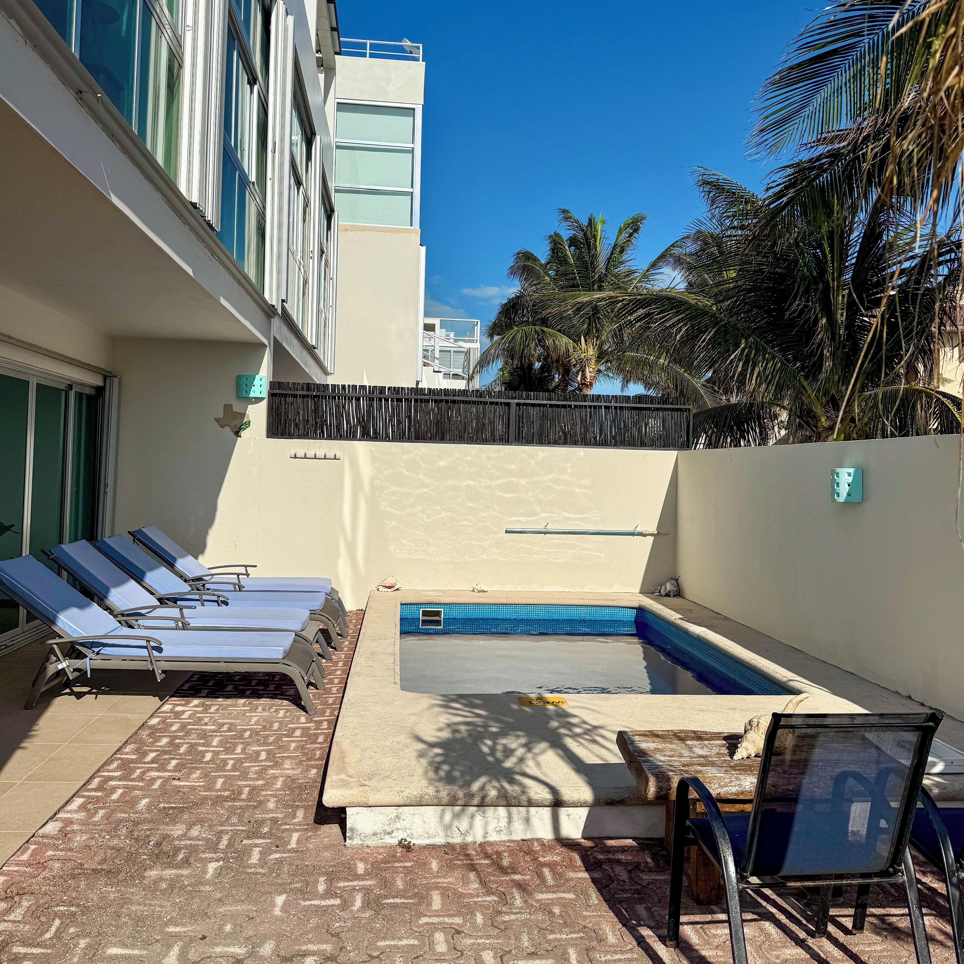 Un área de piscina con sillones de descanso, una piscina pequeña y un patio de ladrillo.