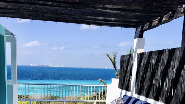 A covered outdoor seating area with a view of the ocean and a city skyline. - Casa Paraiso Caribe - stunning views! (Isla Mujeres)