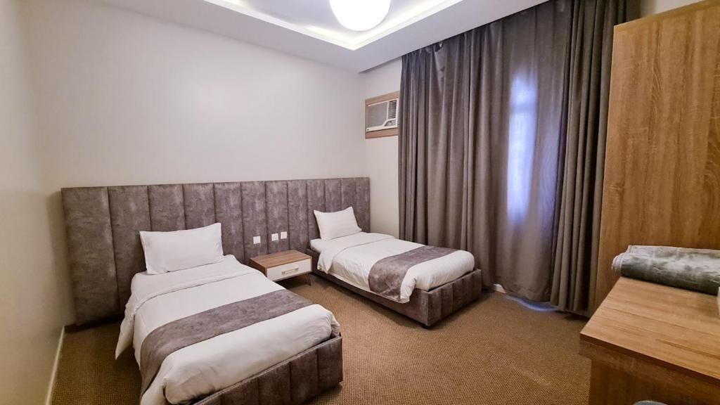 A hotel room with two beds, a desk, a chair, a wardrobe, and a large window with curtains.