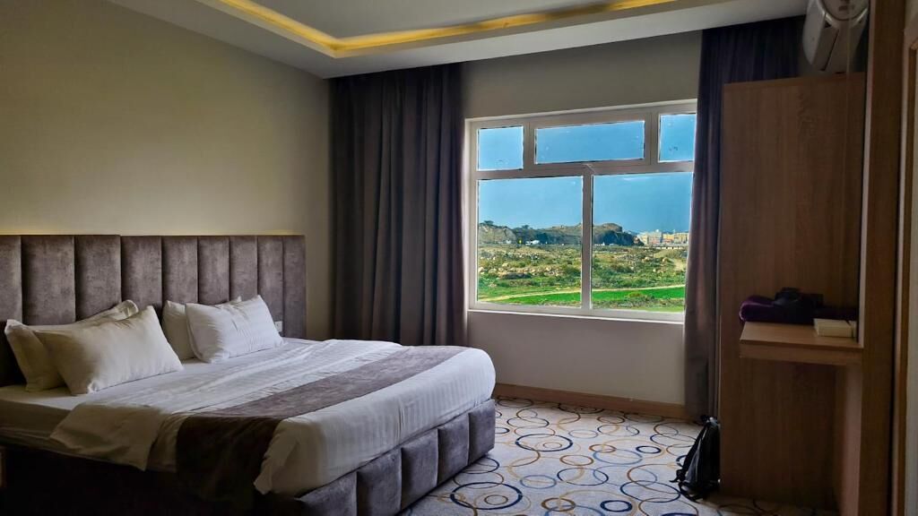 A bedroom with a bed, a window with a view, a wardrobe, and a patterned floor.