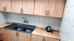 Une cuisine avec des meubles de rangement en bois, un évier à deux bacs et une bouilloire posée sur le plan de travail.