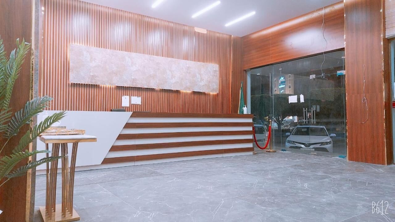 Una zona de recepción con un mostrador de madera, una gran obra de arte abstracta y un acceso de vidrio a un estacionamiento.