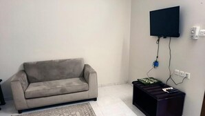 Un salon avec un canapé beige, un tapis à motifs, une table basse noire et un téléviseur à écran plat fixé au mur.