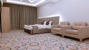 Une chambre d’hôtel avec un lit, deux canapés, une moquette à motifs et une grande fenêtre avec des rideaux.