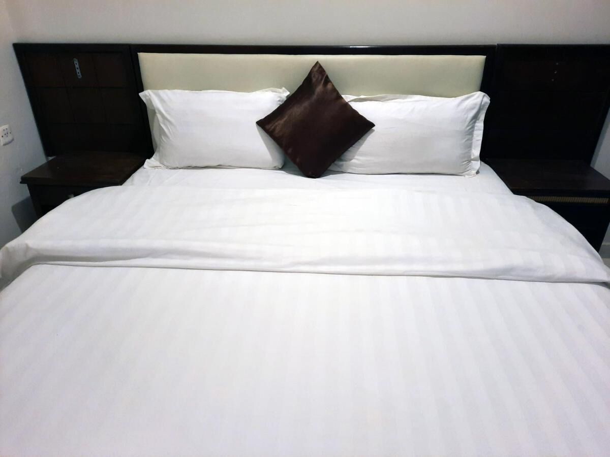 Una cama bien hecha con ropa de cama blanca y una sola almohada marrón.