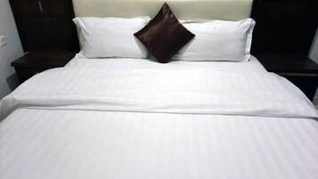 Una cama bien hecha con ropa de cama blanca y una sola almohada marrón.