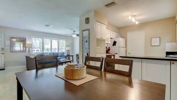 A modern kitchen with white cabinets, a wooden dining table, and a ceiling fan.