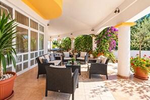 En udendørs patio med fletmøbler, plantede planter og udsigt over det grønne landskab.