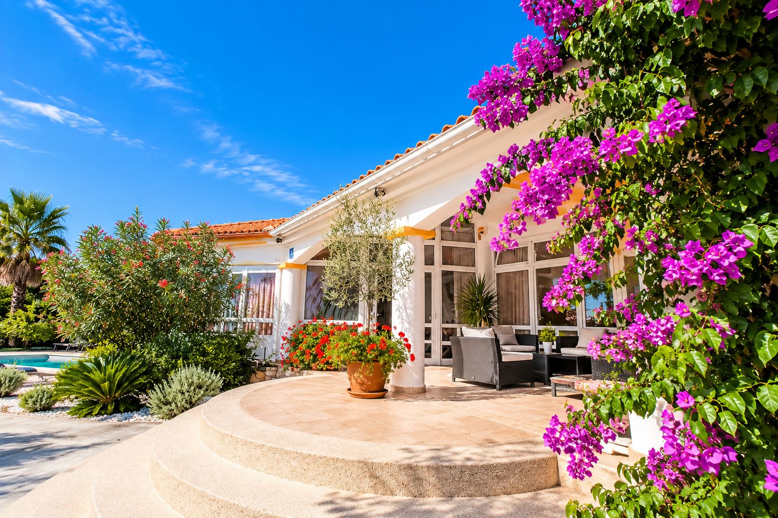 Uma casa com piscina, móveis de exterior e exuberantes flores de buganvillea.
