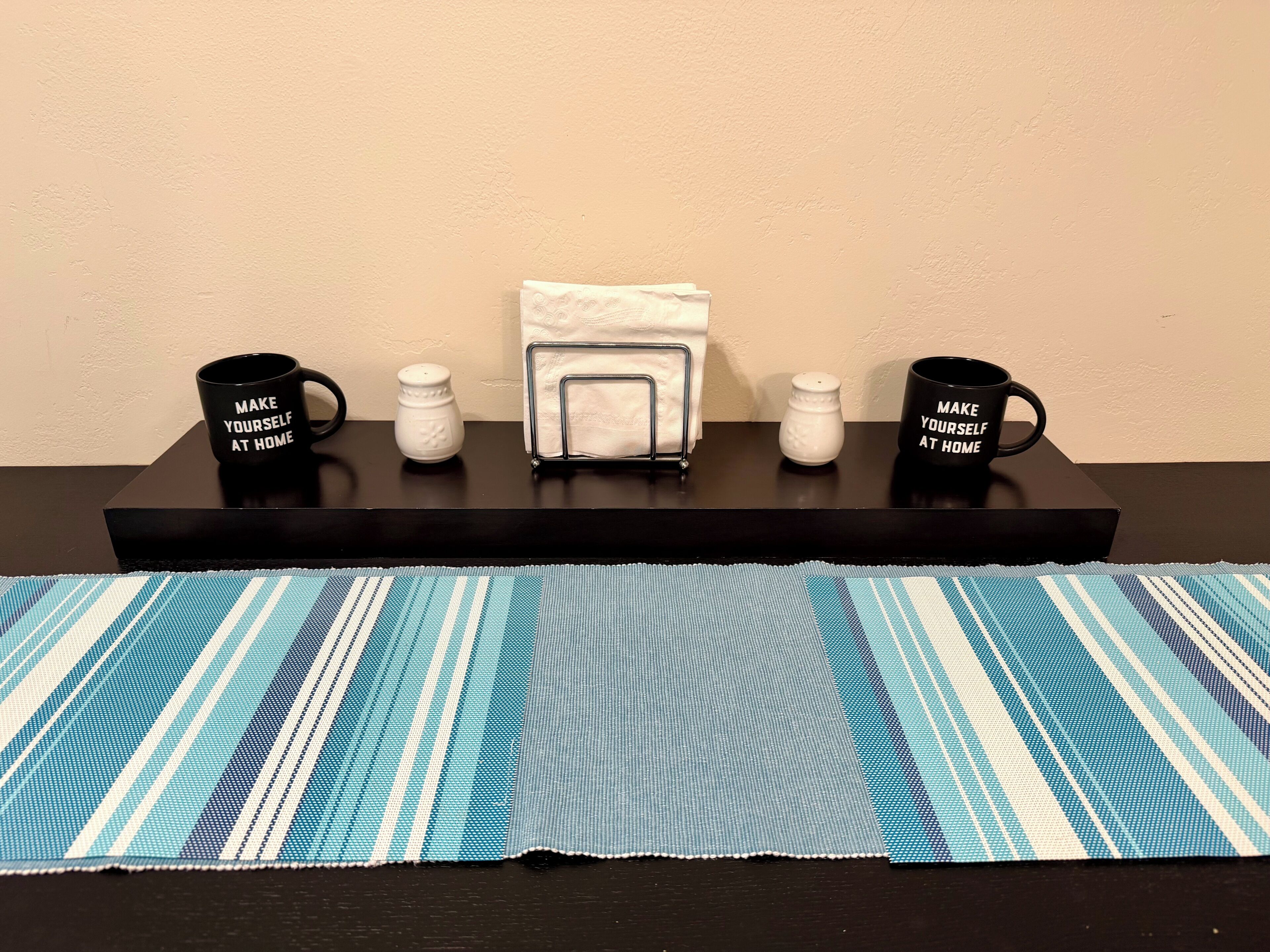Un plateau noir avec deux tasses noires, un salier blanc, un porte-serviettes blanc et une serviette blanche, le tout posé sur une table noire.