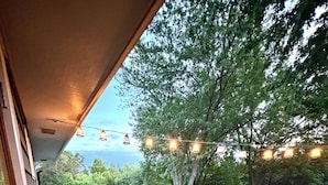 A wooden deck with a railing, a table, and chairs, overlooking a grassy yard with trees and a pool. - Beautiful 2 Bedroom Duplex (Fond du Lac)