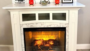 A fireplace with a marble surround, a vase with red flowers, and two framed items on the mantel. - Beautiful 2 Bedroom Duplex (Fond du Lac)