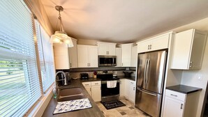 A modern kitchen with white cabinets, stainless steel appliances, a black countertop, and a window with blinds. - Beautiful 2 Bedroom Duplex (Fond du Lac)