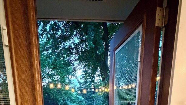 A wooden deck with a railing, a door leading outside, and string lights in the background. - Beautiful 2 Bedroom Duplex (Fond du Lac)