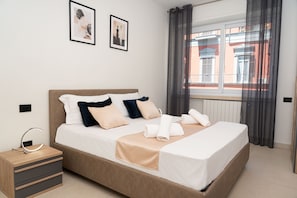 A hotel room with a bed, bedside tables, a nightstand, and a window with curtains.