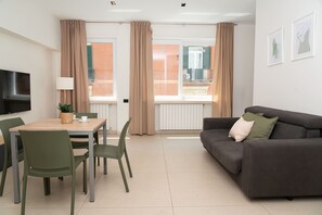A modern living room with a sofa, a dining table with chairs, a flat-screen TV mounted on the wall, and large windows with curtains. - Via Niccolò Tommaseo 4 - appartamento 1 (Napoli)