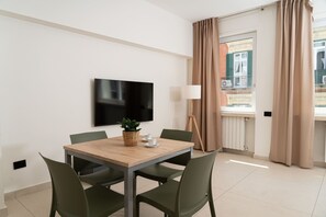 A modern hotel room with a wooden dining table, green chairs, a flat-screen TV, a potted plant, a lamp, and a window with curtains. - Via Niccolò Tommaseo 4 - appartamento 1 (Napoli)