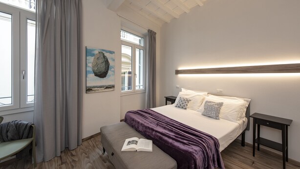 Une chambre à coucher avec un lit, des tables de chevet, un banc et une fenêtre avec des rideaux.