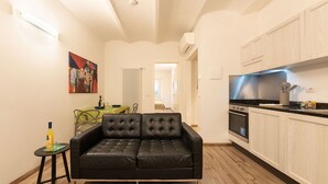 A modern apartment with a black leather sofa, a dining table, and a kitchen area.