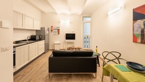 A compact living space with a kitchenette, a black sofa, a dining table with a green tablecloth, and a television.