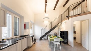 A modern kitchen with a dining area, wooden floors, and a staircase leading to an upper level.