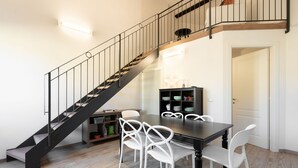 A dining area with a black staircase, white chairs, and a black table.
