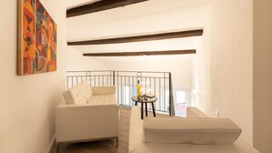 A modern living room with a white sofa, a small round table with a yellow bottle, and a painting on the wall.