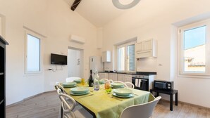 A modern kitchen with white cabinets, a built-in oven, and a microwave. There is a dining table with chairs and a green tablecloth.