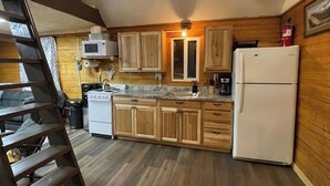 A compact kitchen with wooden cabinets, a stove, a microwave, and a refrigerator. - Rustic Cabin at 17.5 Chena Hot Springs Rd. (Fairbanks)