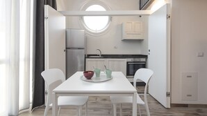 A compact kitchen with white cabinets, a round window, and a dining area with a white table and chairs. - Zannetti 401 Top floor (Firenze)
