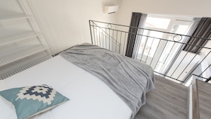 A bedroom with a bed, a grey blanket, a white pillow, a metal headboard, a window with curtains, and a white shelf unit. - Zannetti 401 Top floor (Firenze)