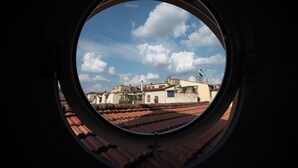 A view through a circular window of a cityscape with terracotta rooftops and buildings under a partly cloudy sky. - Zannetti 401 Top floor (Firenze)