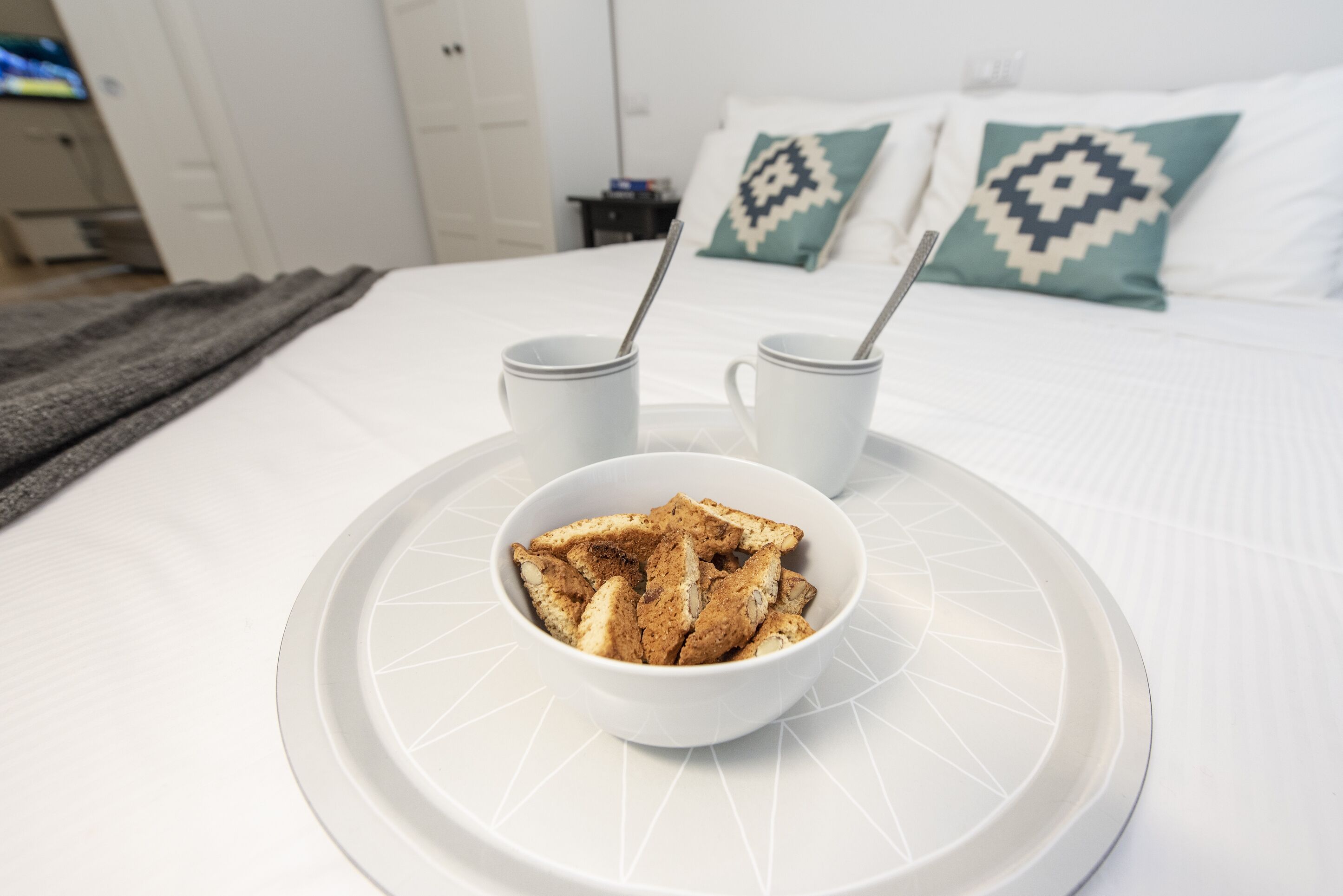 A bed with two white cups and a bowl of cereal on a tray.