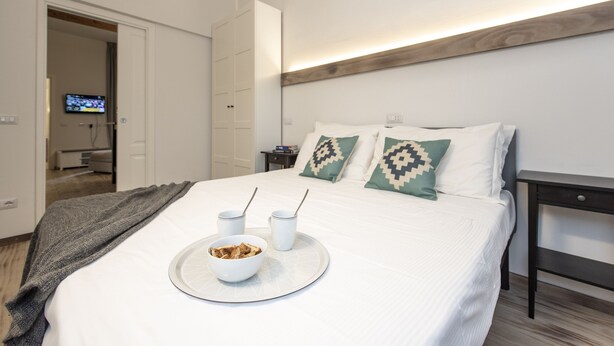 A neatly made bed with a tray of breakfast items, a television in the background, and a modern room design.