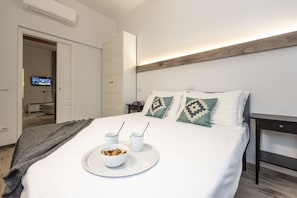 Una cama impecable con una bandeja de desayuno, un televisor al fondo y un diseño de habitación moderno.